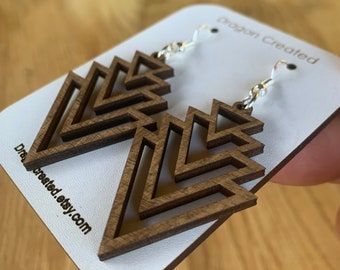 Puede incluir: Un par de pendientes de madera con un diseño geométrico. Los pendientes están hechos de madera oscura y tienen un gancho plateado.