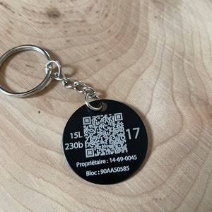 Peut inclure: Porte-clés en métal noir avec un code QR, les numéros 15L, 230b et 17, ainsi que le texte "Propriétaire : 14-69-0045 Bloc : 90AA50585".