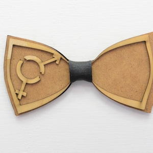 Może przedstawiać: Drewniany krawat muszkowy w kolorze brązowym i czarnym. Muszka ma wycięty wzór symbolu płci.