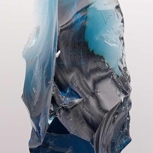 Puede incluir: Escultura abstracta de vidrio en tonos azules y grises. El vidrio es transl&uacute;cido y tiene una superficie irregular y texturizada. Montada sobre una base de acr&iacute;lico transparente.