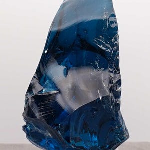 Puede incluir: Una gran pieza de vidrio azul oscuro de forma irregular. El vidrio tiene una cualidad transl&uacute;cida, con &aacute;reas de azul claro y blanco, creando un efecto en capas. Probablemente un objeto decorativo o de arte.