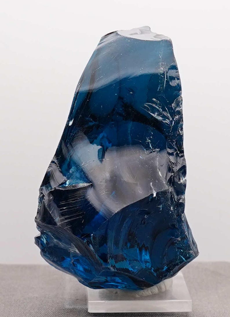 Puede incluir: Una gran pieza de vidrio azul oscuro de forma irregular. El vidrio tiene una cualidad transl&uacute;cida, con &aacute;reas de azul claro y blanco, creando un efecto en capas. Probablemente un objeto decorativo o de arte.