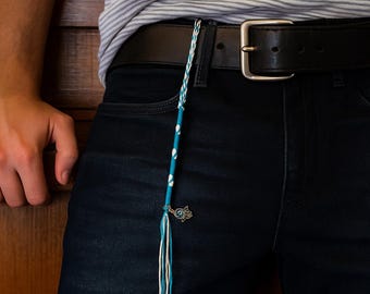 May include: A blue and white braided keychain with a charm. The keychain is hanging from a black belt. The charm is a small, silver-colored design. The keychain has a pattern of white dots on a blue background.
