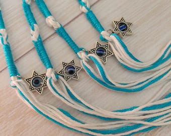 May include: Close-up of several strands of turquoise and white braided cords, each adorned with a silver Star of David charm featuring a blue eye. The cords are arranged in a fan-like pattern.