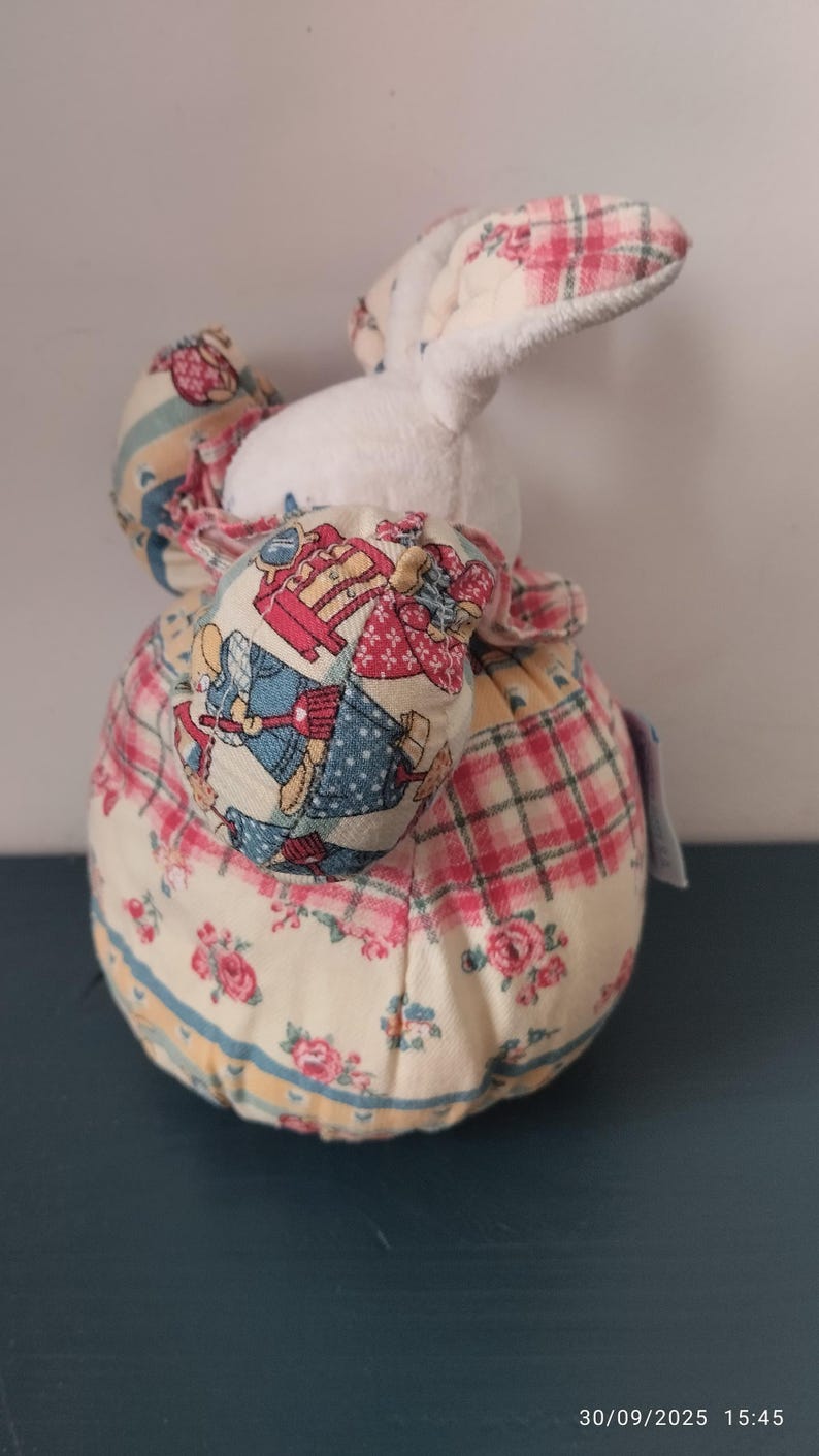 May include: A fabric bunny doorstop with a white body and patterned ears and clothing. The ears have a pink and green plaid design, and the body features floral and patchwork patterns. The doorstop is designed to stand upright.