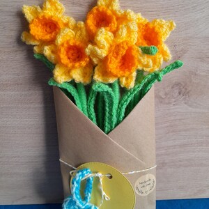 May include: A bouquet of crocheted daffodils in yellow and orange with green stems wrapped in brown paper with a yellow tag that says "handmade with love".
