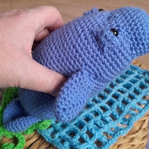 May include: A crocheted blue stuffed animal shaped like a manatee. The manatee is lying on a blue and green crocheted blanket.