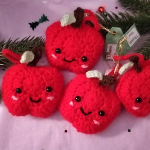May include: Four red crocheted apples with happy faces and green stems. The apples are hanging from gold string with tags that say "Thank You".