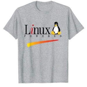 May include: A grey t-shirt featuring a black and white penguin graphic and the text "Linux Powered" in black. The penguin is sitting on a red and orange swoosh.