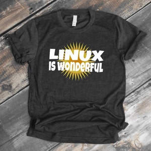 Peut inclure: Un t-shirt gris foncé avec un graphique de soleil blanc et le texte "LINUX IS WONDERFUL" imprimé sur le devant.