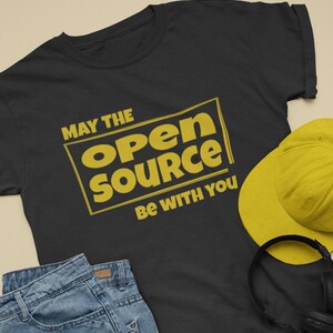 Peut inclure: T-shirt noir avec un graphisme jaune qui dit "Que la source ouverte soit avec vous".