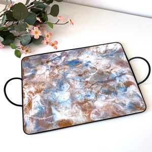 Op de afbeelding: Een witte serveerschaal met bruine en blauwe marmering. De schaal heeft een zwart metalen frame en twee handvatten.