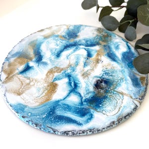 May include: Circular decorative tray featuring a marbled design in blue, white, and gold. The tray has a textured surface and a black and grey border. A decorative item for the home.