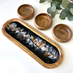 May include: A wooden serving tray with a black and white resin inlay. The tray is accompanied by three smaller wooden bowls.