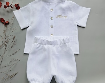 May include: A white short-sleeved shirt with a mandarin collar, four light-colored buttons, and the name Henry embroidered in gold thread on the chest, paired with matching white shorts featuring an elasticized waistband and leg openings.