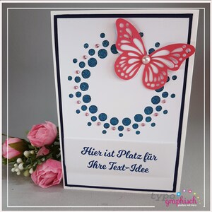 May include: A white card with a blue and pink glitter circle design and a red butterfly with white accents. The card has the text "Hier ist Platz für Ihre Text-Idee" in blue.