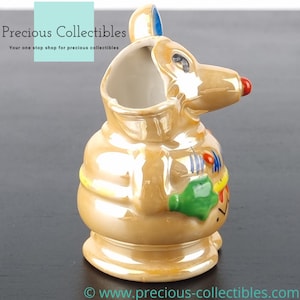 Peut inclure: Une figurine en c&eacute;ramique repr&eacute;sentant une souris avec un gla&ccedil;age brun iridescent. La souris porte une chemise ray&eacute;e jaune et bleue et tient un objet vert et jaune dans sa main. La souris a un nez rouge et des yeux noirs.