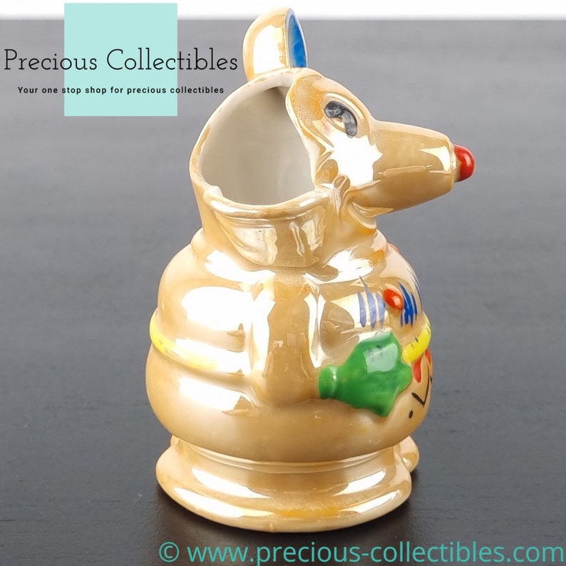 Peut inclure: Une figurine en c&eacute;ramique repr&eacute;sentant une souris avec un gla&ccedil;age brun iridescent. La souris porte une chemise ray&eacute;e jaune et bleue et tient un objet vert et jaune dans sa main. La souris a un nez rouge et des yeux noirs.