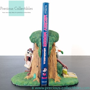 Puede incluir: Un sujetalibros con una representación de dibujos animados de Bugs Bunny y Taz de Looney Tunes. El sujetalibros está hecho de resina y está pintado en colores brillantes. El sujetalibros está sosteniendo un libro titulado "Mickey Mouse Memorabilia" de Abrams.