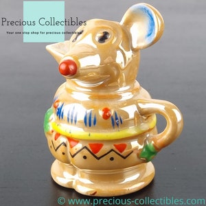 Peut inclure: Un pot &agrave; cr&egrave;me ou une cruche en c&eacute;ramique en forme de souris avec une oreille bleue, un nez rouge et des motifs g&eacute;om&eacute;triques color&eacute;s. Le pot &agrave; cr&egrave;me est glac&eacute; d'une couleur brun clair.