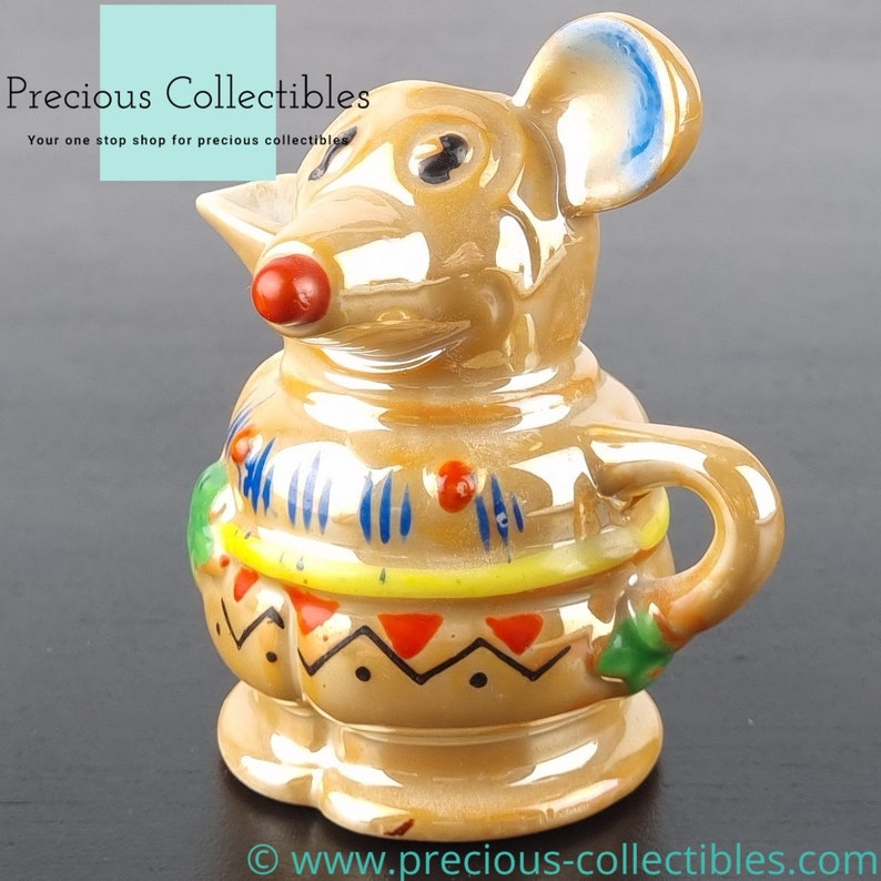 Peut inclure: Un pot &agrave; cr&egrave;me ou une cruche en c&eacute;ramique en forme de souris avec une oreille bleue, un nez rouge et des motifs g&eacute;om&eacute;triques color&eacute;s. Le pot &agrave; cr&egrave;me est glac&eacute; d'une couleur brun clair.