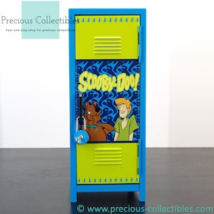 Könnte beinhalten: Ein blauer Metallschließfach mit einem Scooby-Doo!-Design. Das Schließfach hat eine gelbe Tür mit einer Scooby-Doo- und Shaggy-Grafik. Das Schließfach hat ein Zahlenschloss und einen Griff.