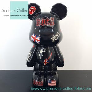 Peut inclure: Figurines d'ours en céramique noire avec un design ressemblant à celui de Mickey Mouse. L'ours est décoré de divers motifs colorés, dont un Union Jack, un drapeau australien et les mots "Rock Star" et "Music is my life".