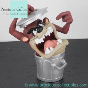 Könnte beinhalten: Eine braune und beigefarbene Figur des Tazmanian Devils mit einem zahnigen Grinsen, die aus einem silbernen Mülleimer mit Deckel herausspringt. Die Figur ist Teil einer Sammlung von Looney Tunes-Charakteren.