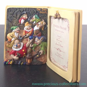 Könnte beinhalten: Cremefarbener Bilderrahmen in Buchform mit 3D-Relief der sieben Zwerge beim Bergbau. Der Rahmen hat eine Fotoöffnung mit Glockenanhängern und den Text "Photo Frame". Größe: 8cm x 12cm.