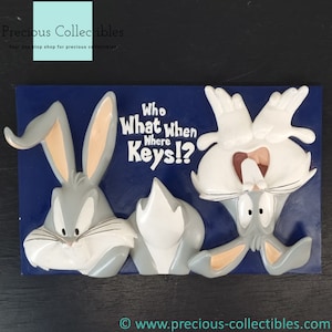 Könnte beinhalten: Eine blaue und graue Wandplakette mit drei Bugs Bunny-Charakteren. Die Plakette trägt den Text "Who What When Where Keys!?"