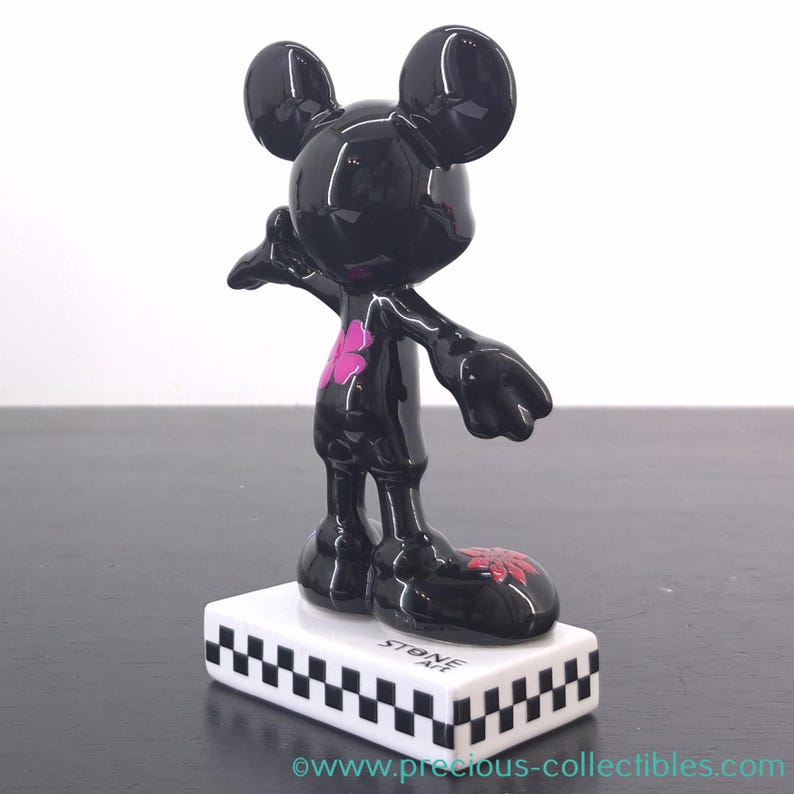 May include: Black Mickey Mouse figurine with a glossy finish, featuring a pink flower design on the chest and feet. The figurine stands on a white base with a black and white checkered pattern and the text "STONE ART".
