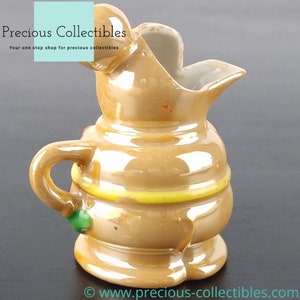 Peut inclure: Un petit pichet en c&eacute;ramique brun avec un motif jaune et vert. Le pichet a un bec verseur et une anse.
