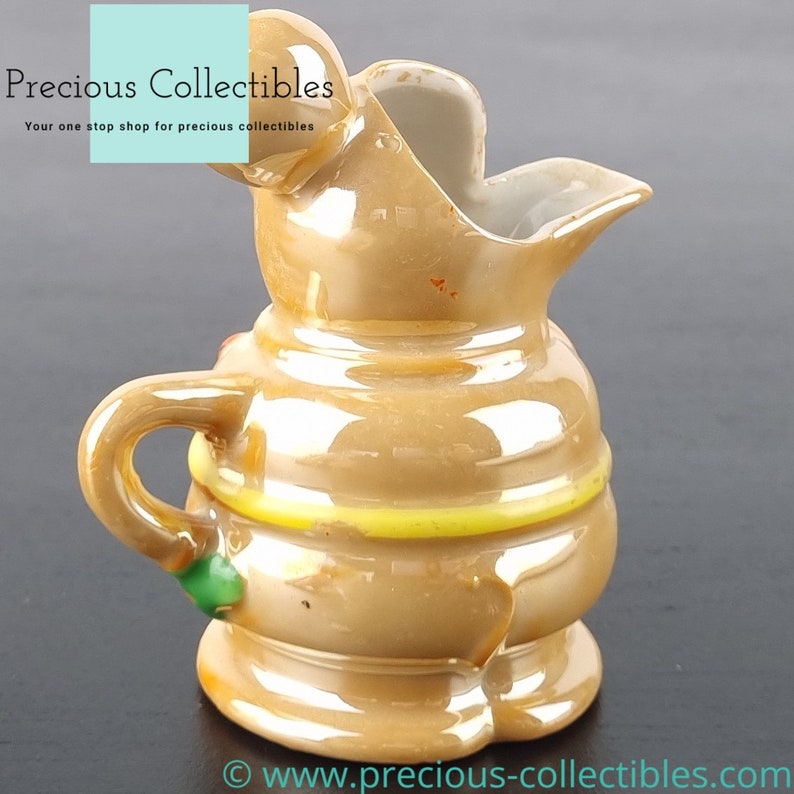 Peut inclure: Un petit pichet en c&eacute;ramique brun avec un motif jaune et vert. Le pichet a un bec verseur et une anse.