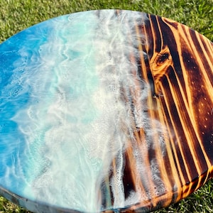May include: A round wooden table top with a blue and white epoxy resin design on one half and a burnt wood finish on the other half.