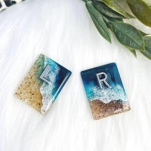 May include: Two small resin squares with a beach scene and glitter. The squares have the letters "L" and "R" in silver.