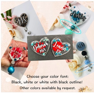 May include: A collection of personalized heart-shaped badge reels and a round badge reel. The heart-shaped reels feature names and floral designs in various colors. The text on the image reads, "Choose your color font: Black, white or white with black outline! Other colors available by request."