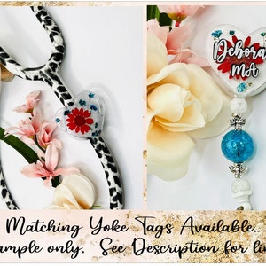 May include: A stethoscope with a black and white spotted design, paired with a heart-shaped badge reel. The badge reel features a red flower and the name "Deborah MA". The image also includes text that reads "Matching Yoke Tags Available. Example only. See Description for link."