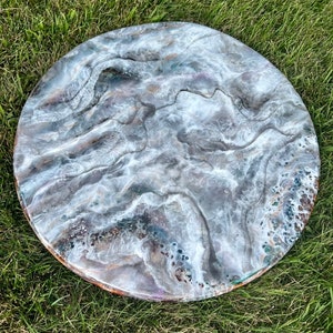 May include: A round, white resin table top with a swirling, marbled pattern in shades of gray, brown, and white. The table top has a smooth, glossy finish.
