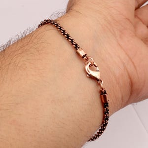 Könnte beinhalten: Ein Kupferkettenarmband mit einem Karabinerverschluss.