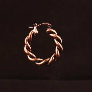 May include: A single hoop earring crafted from a metallic copper-toned material, featuring a distinct twisted rope design. The circular earring includes a hinged post mechanism at the top, allowing it to open and close securely for wear.