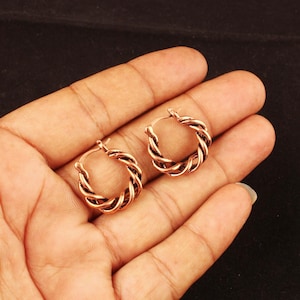 May include: A pair of small hoop earrings crafted from copper-toned metal. Each earring features a twisted, rope-like design that creates a textured, circular shape. The earrings have a metallic finish with visible dark oxidation in the crevices.