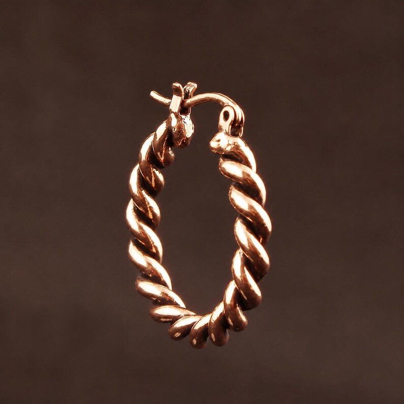 May include: A single hoop earring crafted from polished rose gold-toned metal, featuring a continuous twisted rope design. The earring includes a hinged post mechanism at the top, allowing it to open and close securely for wear in a pierced earlobe.
