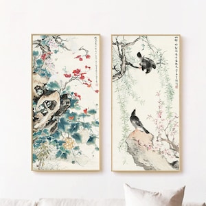 May include: Two framed paintings with a white background. The paintings feature traditional Chinese brushstrokes and depict birds perched on branches with flowers. The paintings are hung on a white wall above a white couch.