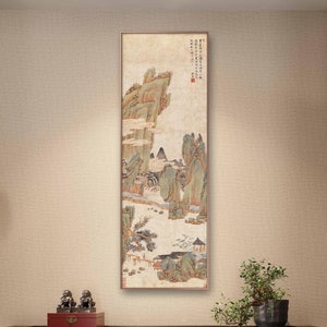 May include: A framed painting of a traditional Chinese landscape scene with mountains, trees, and a small village. The painting is done in shades of green, brown, and white, and the frame is a simple, light brown wood.