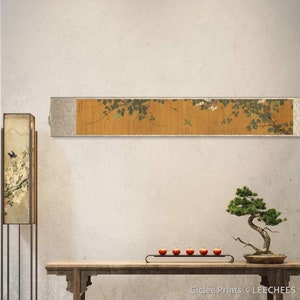 May include: A traditional Japanese scroll painting depicting a branch of a flowering tree with delicate white blossoms and green leaves. The scroll is mounted on a wall in a modern interior with a wooden table, a bonsai tree, and a lamp.