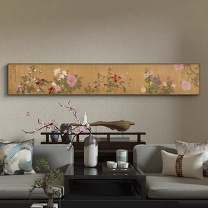 Peut inclure: Une longue peinture horizontale représentant un arrangement floral avec des fleurs roses, blanches et rouges sur un fond doré. La peinture est accrochée au mur au-dessus d'un canapé gris avec des coussins et une table basse.
