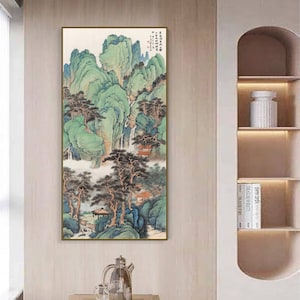 May include: A framed painting depicting a traditional Chinese landscape with green mountains, trees, and a waterfall. The painting is in a gold frame and is hanging on a wall.