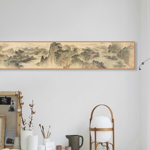 May include: A long, horizontal painting depicting a traditional Chinese landscape scene with mountains, trees, and water. The painting is framed in a simple wooden frame and hangs on a white wall.
