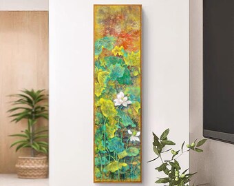 May include: Vertical wall art featuring a painting of lotus flowers and leaves. The artwork has a gold frame and a textured background with shades of yellow, green, and red. Two white lotus flowers are visible among the green leaves.