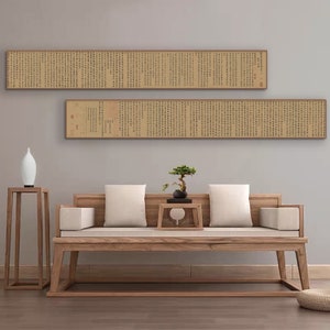 May include: Two long, horizontal scrolls with black text on a beige background are framed in wood and hung on a light gray wall. A wooden couch with white cushions sits in front of the scrolls. A small potted bonsai tree sits on a wooden table in front of the couch.